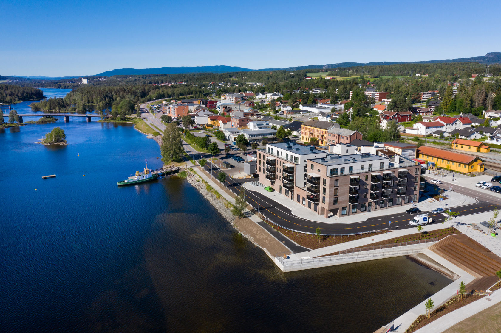 Dronefoto med vannet i forgrunn, prosjektet og togstasjonen like bak prosjektet