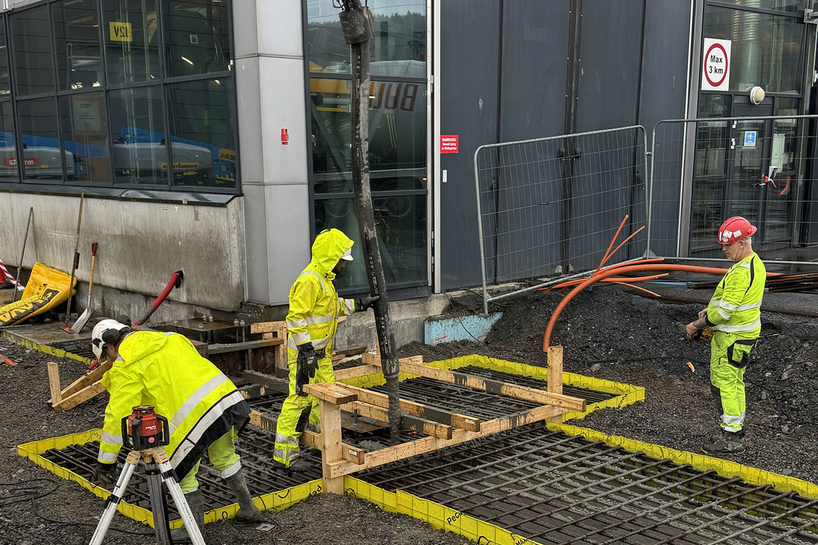 Tre personer i arbeid med støping, betongen pumpes i slange ned i armering og forskaling.
