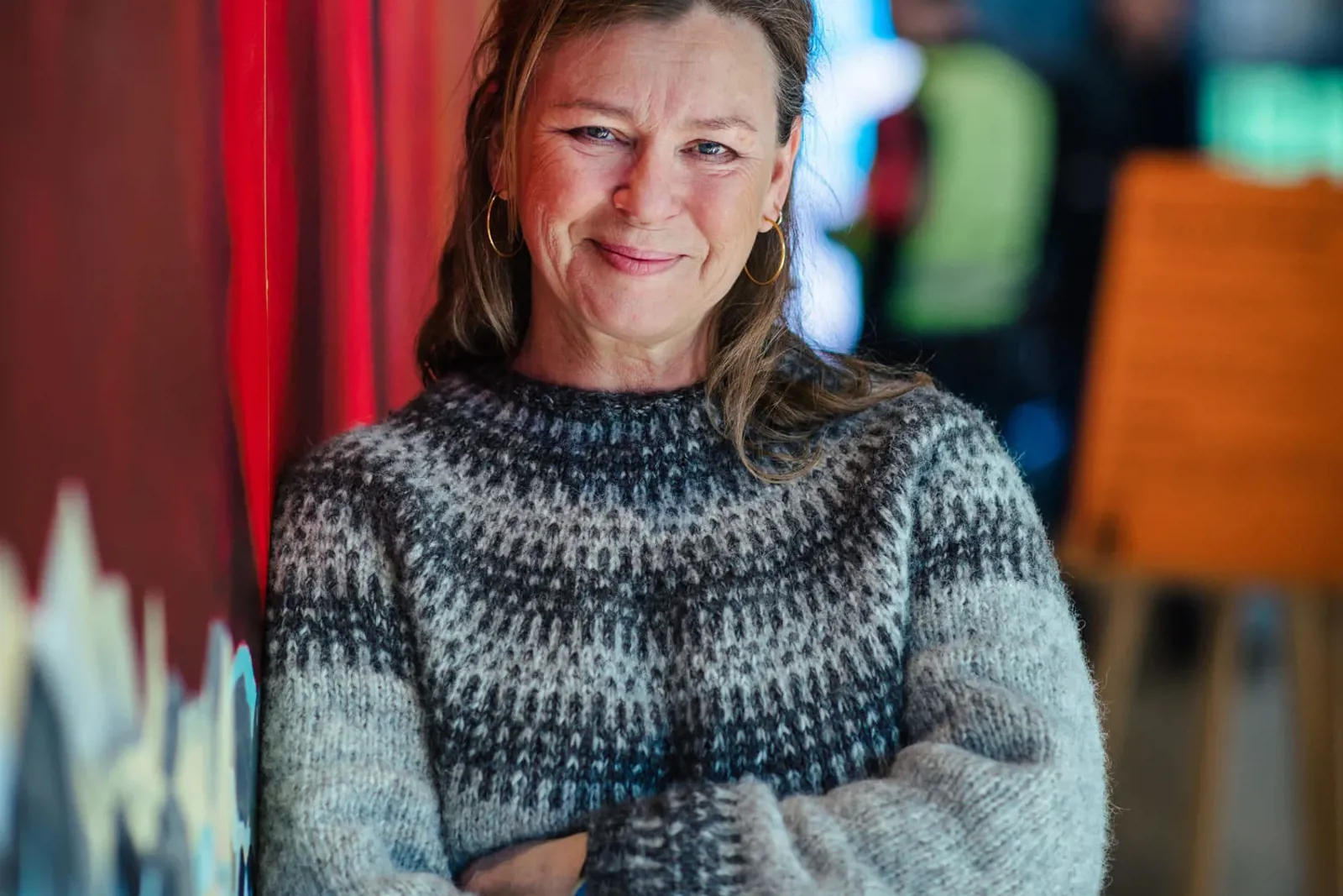 Portrettbilde av smilende dame med strikkegenser og armene i kors. Fargerik bakgrunn.