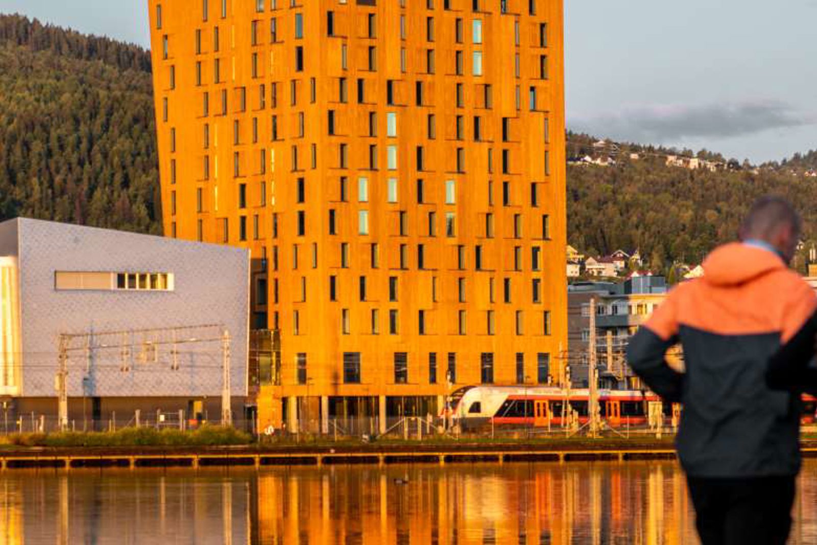 I bakgrunn: hotell, næringsbygg og togstasjon. I forgrunn: to mennesker som jogger.