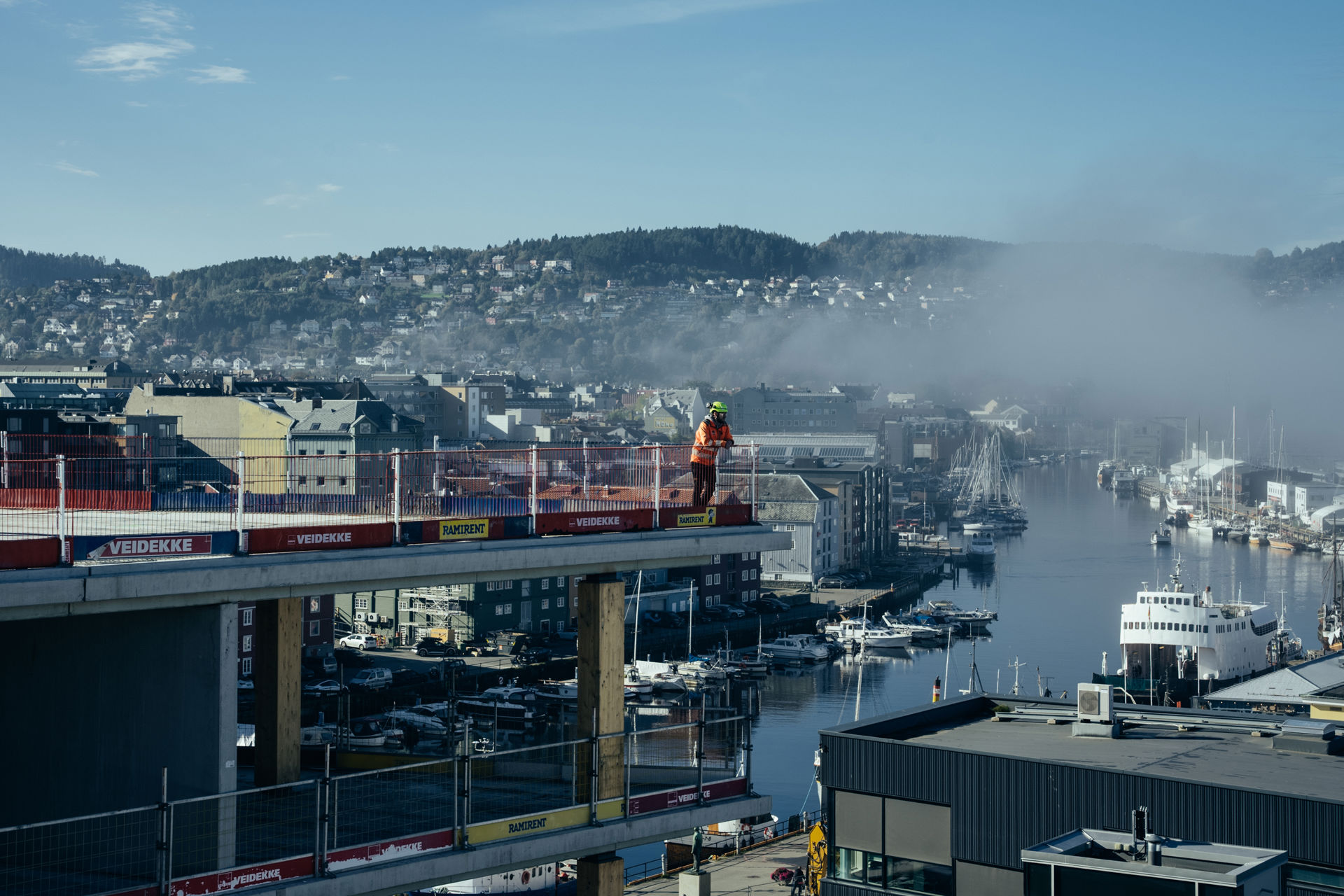 Utsikt til et bygg som er under bygging. Tåke i luften og utsikt til Nidelven.